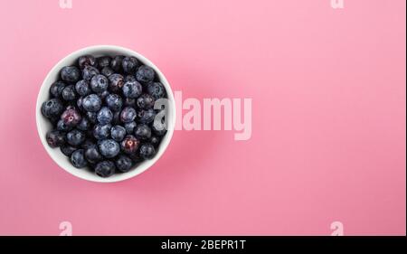 vue sur un petit bol de poterie blanche rempli de bleuets mûrs frais sur la surface de la table rose Banque D'Images