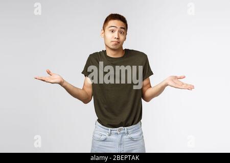 Qui sait, je ne sais pas. Portrait d'un homme asiatique haussant et confus dans un t-shirt greey, sauté et excusant, désolé de ne pas pouvoir aider, debout perplexe et Banque D'Images