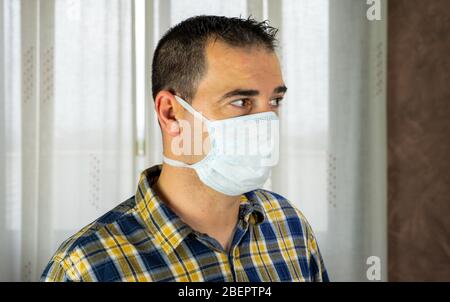 Homme posant avec masque dans le salon de sa maison se protégeant du covid-19 Banque D'Images