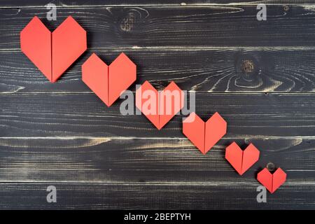 Coeurs rouges d'origami de différentes tailles en composition sur fond noir en bois abîmé Banque D'Images