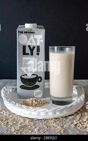 Oatly végétalan Oat Drink Barista Edition en verre avec carton derrière sur plateau peint blanc avec avoine parsemée autour et fond noir. Utilisation éditoriale o Banque D'Images