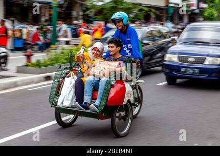 Taxi et passagers de moto, rue Malioboro, Yogyakarta, Indonésie. Banque D'Images