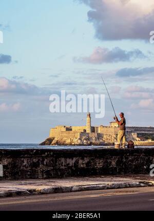 Homme pêchant à El Malecon, le château El Morro et le phare en arrière-plan, coucher de soleil, la Havane, la province de la Habana, Cuba Banque D'Images