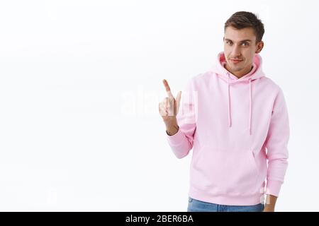 Portrait de l'homme blond Sassy dans le sweat à capuche rose, en pointant le doigt dans le coin supérieur gauche et souriant, en invitant à vérifier l'offre ou la remise promotionnelle Banque D'Images