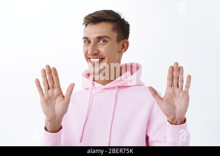 Non merci, je vais bien. Portrait de beau homme blond souriant dans le hoodie rose, levant les mains en reddition ou geste désolé, refuser ou rejeter l'offre Banque D'Images