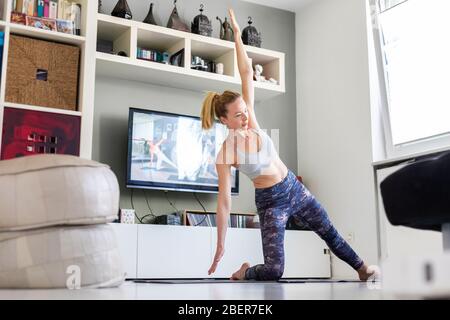 Jolie femme sportive travaillant à la maison, faisant des pilates exercice devant la télévision dans son salon. Distanciation sociale. Restez en bonne santé et Banque D'Images