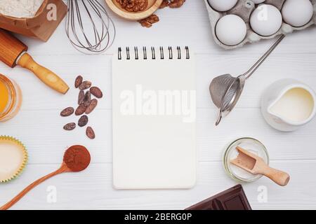 Ingrédients et ustensiles pour la boulangerie ou la fabrication de dessets et de bloc-notes en papier blanc sur la table blanche. Banque D'Images