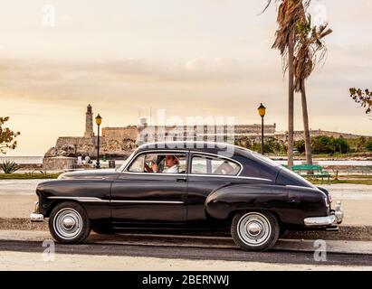 Cigare modèle cubain fumage dans sa voiture Chevrolet d'époque à El Malecon, Château El Morro en arrière-plan, la Havane, la province de la Habana, Cuba (MR) Banque D'Images