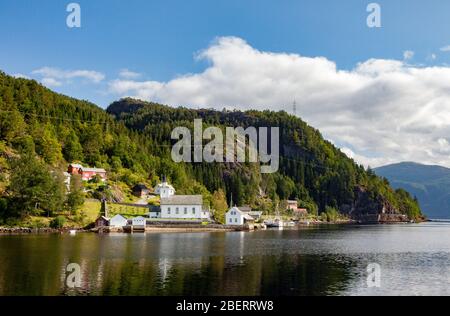 Un petit village avec maisons et bâtiments blancs est situé au bord de l'Osterfjord en Norvège, près de Bergen, sous un ciel bleu avec des nuages blancs Banque D'Images