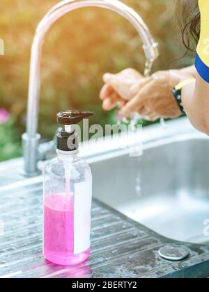 Une femme se lavant les mains du robinet avec du savon rose dans une baignoire en aluminium. Concepts du virus de la grippe, Covid-19 (maladie du coronavirus). Focalisation sélective sur le savon b Banque D'Images