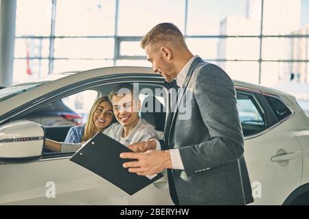 Un couple heureux teste une nouvelle automobile avant de signer un contrat de vente de véhicules. Banque D'Images