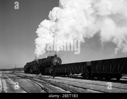 Un train à vapeur dans une cour de train soufflant des nuages de fumée ciel haut. Banque D'Images