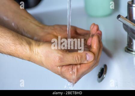 Gros plan homme lave ses mains, l'eau du robinet verse sur les mains de la mans Banque D'Images