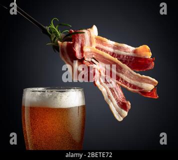Bière et tranches de bacon frit savoureux garnies de romarin. Banque D'Images