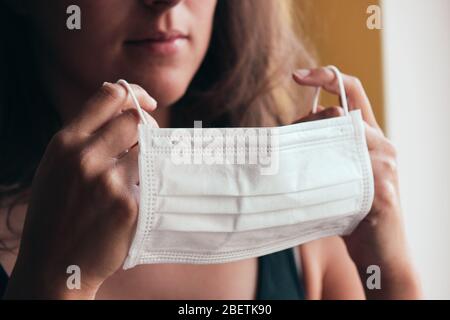 Photo détaillée d'une femme blanche non reconnaissable mettant sur un masque médical blanc pour prévenir l'infection. Fond flou, foyer sur le masque. Coronavirus, COVID-19 quarantaine. Concept de verrouillage. Banque D'Images