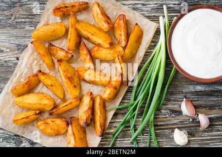 Pommes de terre dorées épicées frites ou cuites à l'ail, à la sauce et à l'oignon sur une table en bois. Délicieux en-cas savoureux et croustillants dans un style rustique. Vue de dessus. Banque D'Images