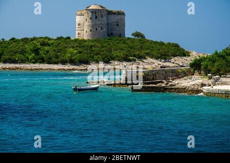 Bateau de pêche près du monastère et de l'église sur l'île et la forteresse Arza près de Zanjic sur la péninsule de Lustica, baie de Boka Kotor avec eau bleue turquoise paradisiaque Banque D'Images