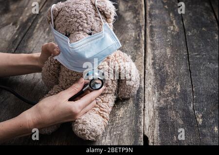 Image conceptuelle de la main pédiatrique - femme tenant le stéthoscope médical sur l'ours en peluche avec masque de protection. Banque D'Images