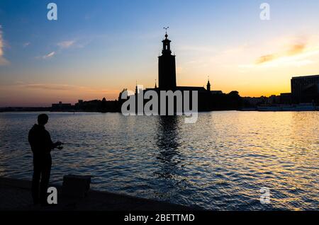 Silhouette de pêcheur avec poteau de pêche et de Stockholm Hôtel de ville Stadshuset bâtiment Conseil municipal sur l'île Kungsholmen au coucher du soleil, crépuscule, crépuscule Banque D'Images