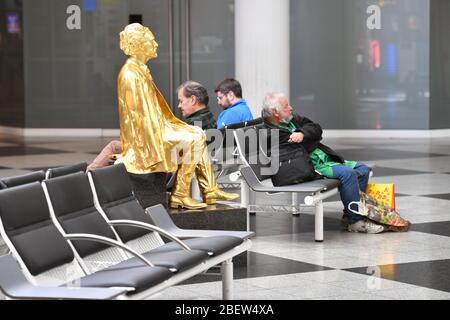 Photo thématique pandémie de coronavirus le 15 avril 2020. Aéroport Franz Josef Strauss de Munich. Aéroport de Munich. Peu de voyageurs sont assis à côté d'une statue dorée. | utilisation dans le monde entier Banque D'Images