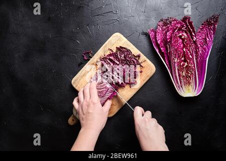 Chou rouge chinois haché (wombok violet) sur planche à découper en bois sur table en pierre noire. Chou rouge Napa avec des feuilles de couleur vive sur le noirceur Banque D'Images