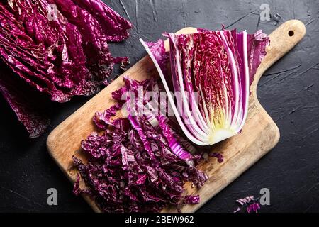 Chou rouge chinois haché (wombok violet) sur planche à découper en bois sur table en pierre sombre. La moitié du chou rouge Napa sur fond noir, vue de dessus. Cuisine Banque D'Images
