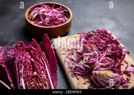 Chou rouge chinois haché (wombok violet) sur planche à découper en bois et bol sur table en pierre. Chou rouge Napa avec des feuilles de couleur vive sur le bac noir Banque D'Images