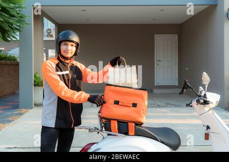 Livraison Asian homme portant l'uniforme orange et prêt à envoyer livraison sac alimentaire devant les clients houes avec boîte case sur scooter, express food deli Banque D'Images