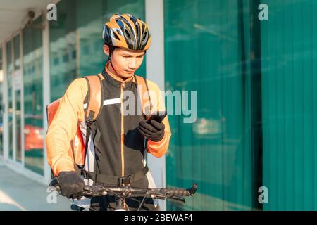 Messagerie asiatique homme vérifiant l'adresse du client sur la carte dans smartphone sur la bicyclette livrant la nourriture dans les rues de la ville avec une livraison de nourriture chaude de prendre des aways A Banque D'Images