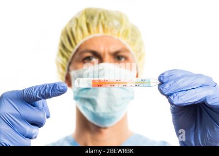 médecin en vêtements médicaux avec gants en caoutchouc et masque, le portrait sur fond blanc pointe vers un thermomètre à haute température. Banque D'Images