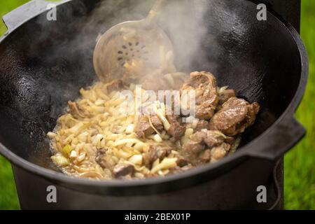 Cuisine de savoureux pilaf dans un chaudron en fonte. Viande de mouton frite avec oignon à kazan. Banque D'Images