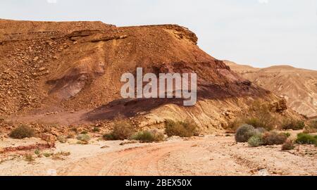 petite falaise sur wadi ardon dans makhtesh ramon en israël montrant des détails de la géologie du cratère avec une route à quatre roues motrices en premier plan Banque D'Images