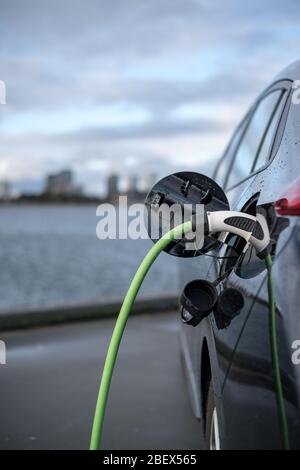 11-20-2020, Copenhague, Danemark - charge d'une voiture électrique, avec la ville et l'eau en arrière-plan, le câble de chargement vert et la voiture noire. copenhague Banque D'Images