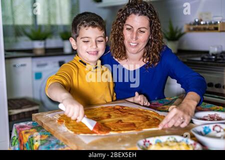 Enfant mettant de la sauce tomate sur une pizza maison Banque D'Images