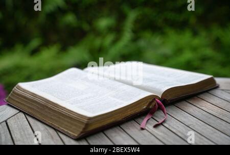 Ouvrir la bible sur la table en bois. Effet flou doux avec mise au point sur le repère du livre. Nature verte en arrière-plan. Banque D'Images