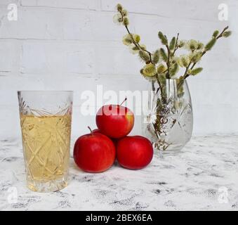 pommes de composition biologiques à branche saule. Plusieurs pommes rouges mûres et jus de pomme se trouvent sur une table blanche près d'un vase en cristal avec saule Banque D'Images