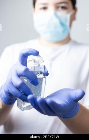 garçon avec masque de protection et gants bleus se laver les mains avec de l'alcool pendant la quarantaine du coronavirus Banque D'Images