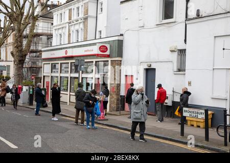 Kilburn, Londres, Royaume-Uni, 4 avril 2020 une file d'attente à l'extérieur d'un bureau de poste tandis qu'une politique de mise en place de distanciation sociale est en place pendant le virus Covid-19. Banque D'Images