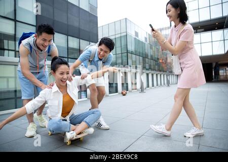 Le jeune homme pousse la femme classmate assis sur un skateboard Banque D'Images