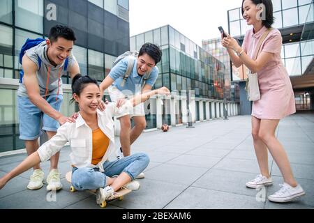 Le jeune homme pousse la femme classmate assis sur un skateboard Banque D'Images
