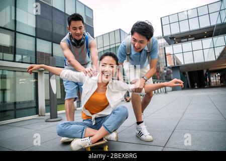 Le jeune homme pousse la femme classmate assis sur un skateboard Banque D'Images