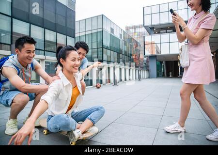 Le jeune homme pousse la femme classmate assis sur un skateboard Banque D'Images
