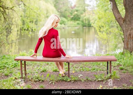 Blonde femme portant un bureau assis sur un banc dans le parc près d'un lac. L'image reflète le retour à la vie naturelle Banque D'Images