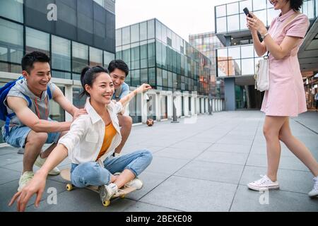 Le jeune homme pousse la femme classmate assis sur un skateboard Banque D'Images