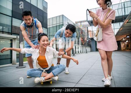 Le jeune homme pousse la femme classmate assis sur un skateboard Banque D'Images