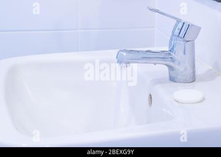 l'eau du robinet coule avec du savon sur le bassin blanc dans l'intérieur de la salle de bain Banque D'Images