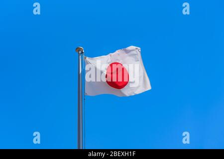 Drapeau national japonais se fouitant au vent contre un ciel bleu ensoleillé. Banque D'Images