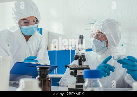 foyer sélectif de deux biochimistes qui tiennent des boîtes de petri près du microscope et des contenants médicaux Banque D'Images