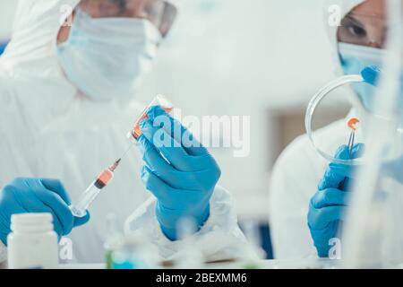 foyer sélectif de biochimiste prenant des médicaments avec seringue près de collègue tenant la boîte de petri Banque D'Images