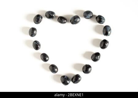Raisins noirs disposés en forme de coeur d'amour sur un fond blanc Uni Banque D'Images